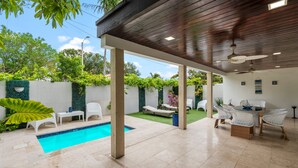 Ein Außenpoolbereich mit einer Holzpergola, weißen Liegestühlen und einem Essplatz.