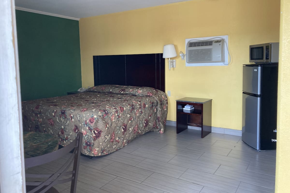 A hotel room with a bed, a small bedside table, a microwave, and a refrigerator.