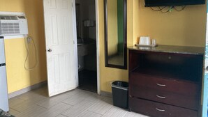 A hotel room with a white door, a mirror, a TV mounted on the wall, a small trash bin, and a dresser with drawers. - Capri motel (Alice)