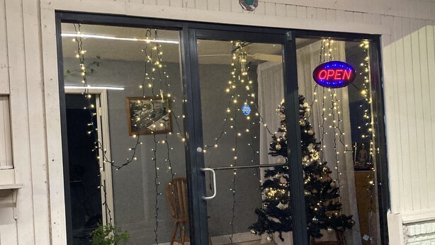 A storefront with a glass door, decorated with string lights and a Christmas tree. - Capri motel (Alice)