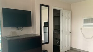 A room with a dark dresser, a flat-screen TV mounted on the wall, a white door leading to a closet, and a wall-mounted air conditioning unit. - Capri motel (Alice)