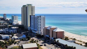 A coastal cityscape with a prominent hotel featuring a modern design, a beachfront, and surrounding urban buildings.