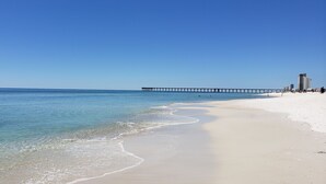 A beach with a pier extending into the water, clear skies, and a few people on the sand.