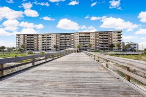 A wooden boardwalk leading to a modern apartment building with multiple balconies and a clear blue sky.