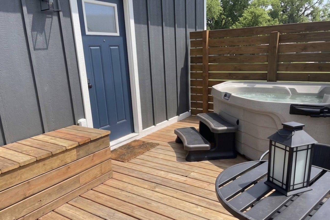 A wooden deck with a hot tub, steps, and a table with a lantern.