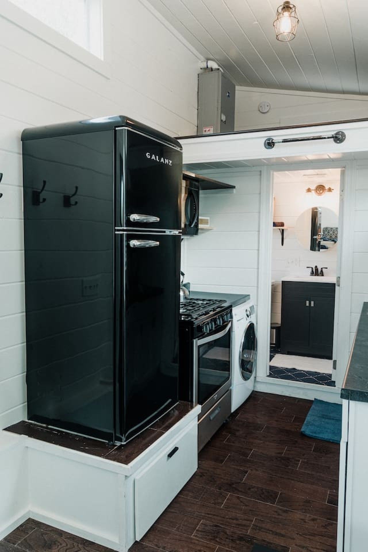 Una cocina compacta con un refrigerador negro, estufa y lavadora.