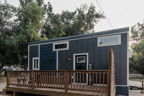 A small, dark-colored building with a wooden deck and a 'WE' sign, surrounded by trees.