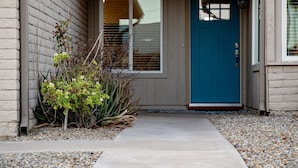 A house with a blue door, a concrete pathway, and a small garden with plants and rocks. - 4BR w pool, shuffleboard, 2 king rooms (Chandler)