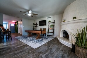 A living room with a fireplace, a dining table, and a TV mounted on the wall. - Shuffleboard! Heated Pool! Live w/ 2 Kings Cool! (Chandler)