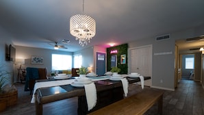 A modern kitchen with a wooden dining table set for four, a chandelier, and a green wall with a neon sign. - 4BR w pool, shuffleboard, 2 king rooms (Chandler)