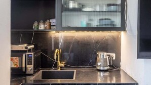 A kitchen with a black countertop, a sink, a coffee maker, and a microwave. - Nissim (Jerusalem)