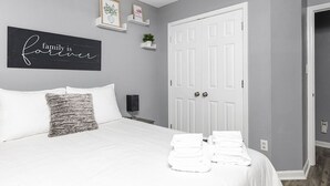 Une chambre à coucher bien rangée, avec un lit, des oreillers, une table de chevet, une lampe, une porte et un panneau accroché au mur.