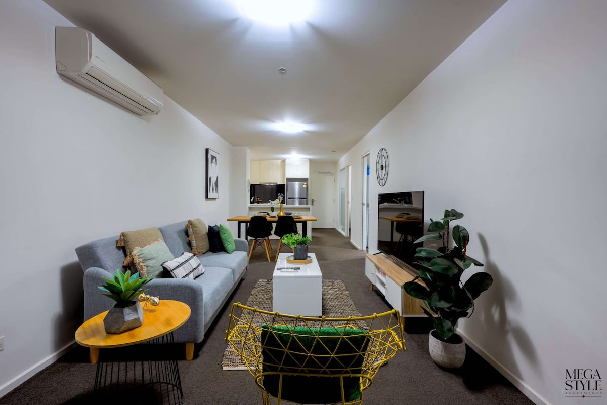A modern living room with a sofa, coffee table, and a dining area in the background.
