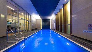 An indoor swimming pool with clear glass walls, a no diving sign, and a pool depth sign.