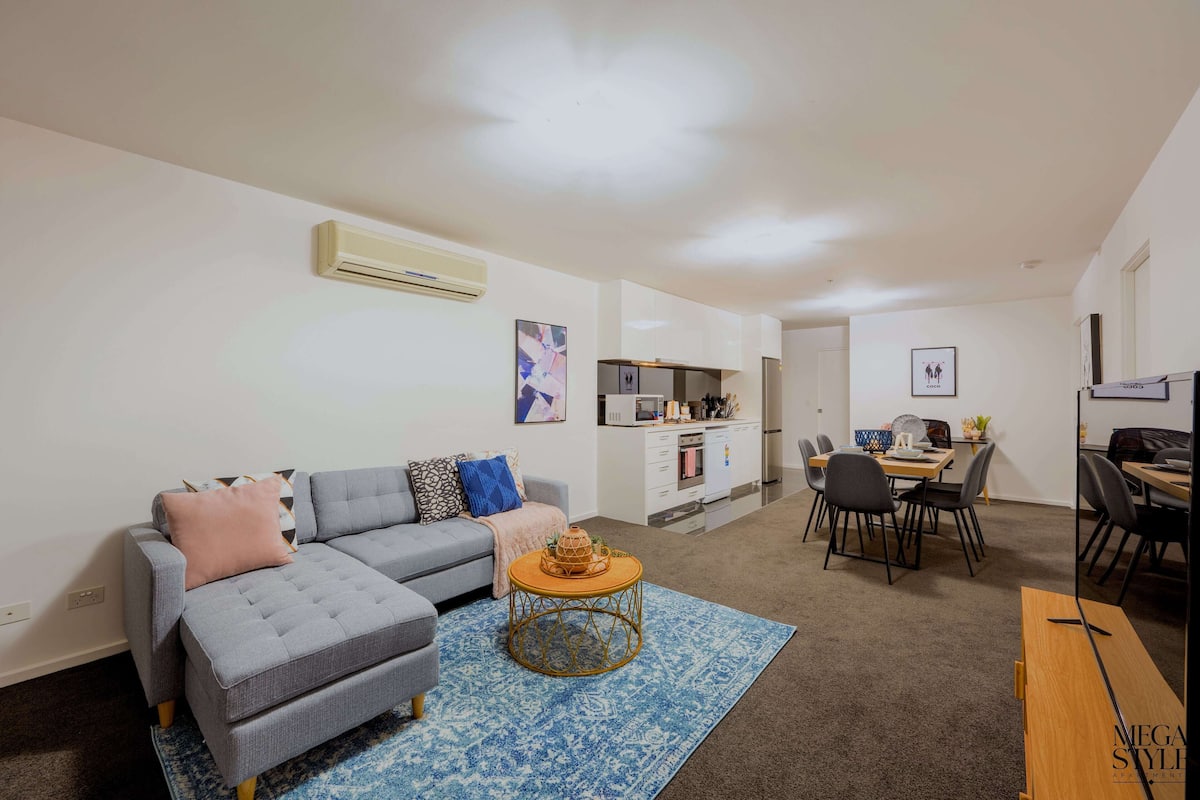 A modern living room with a grey sectional sofa, a round coffee table, and a dining area with a table and chairs.