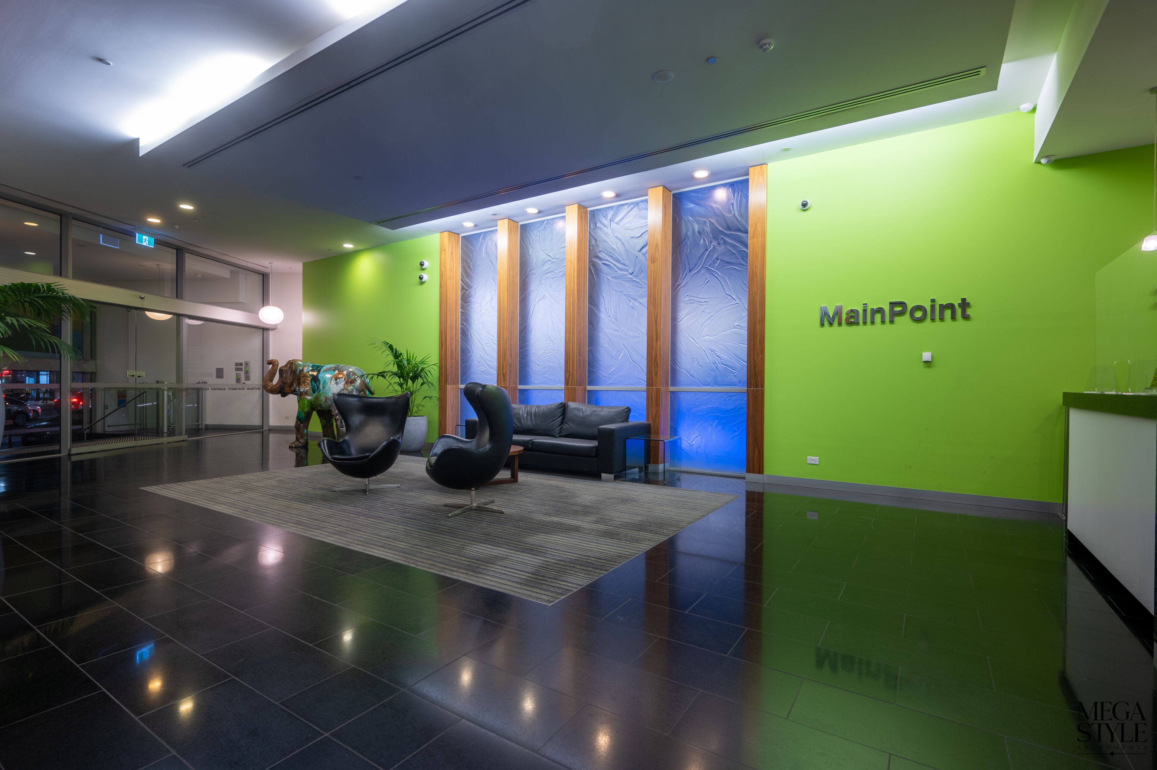 A modern lobby with a green accent wall, a reception desk, and a seating area with black chairs and a sofa.