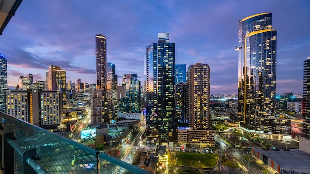 A cityscape at dusk with illuminated skyscrapers and a busy street below.