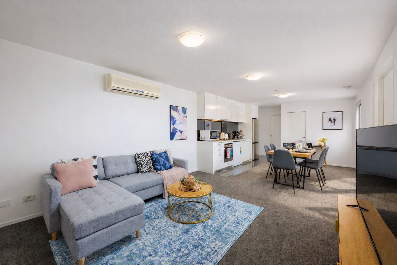 Un appartement moderne avec un canapé gris, un coin repas et une cuisine.