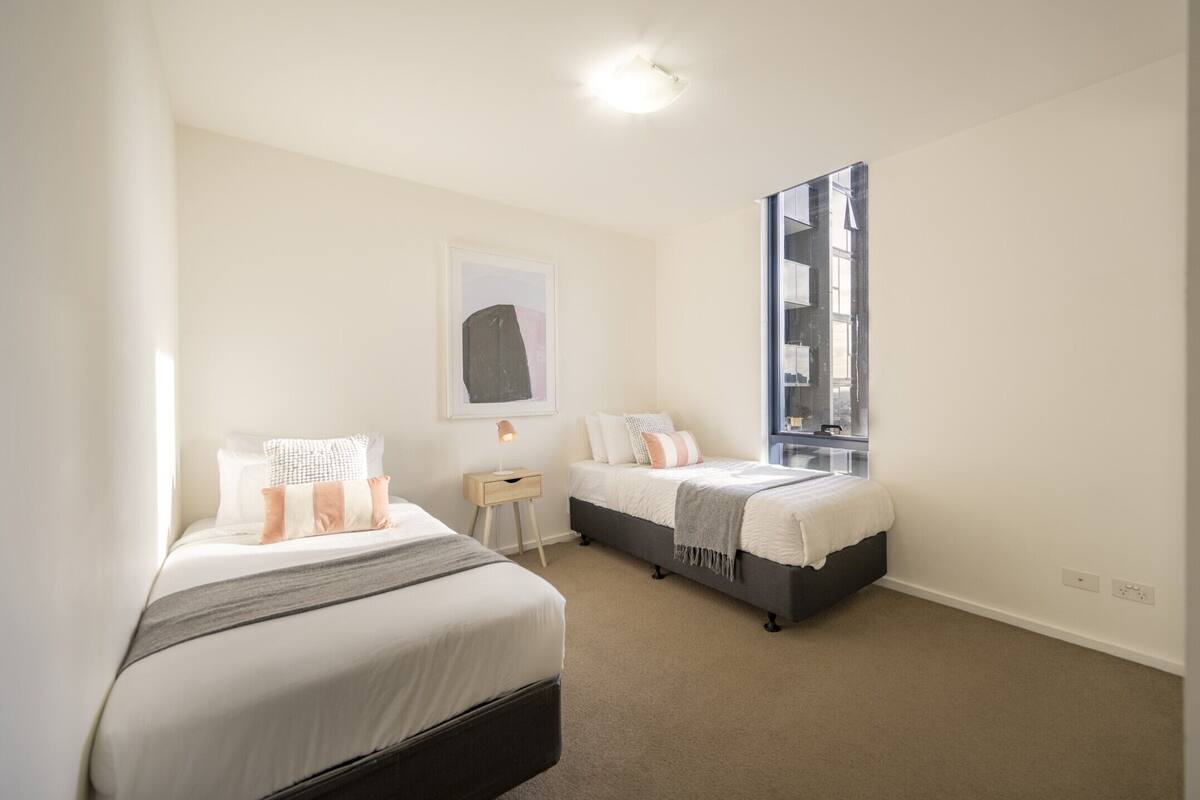A bedroom with two beds, a nightstand, a mirror, and a window.