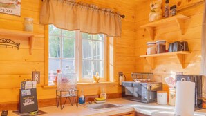 Une cuisine rustique aménagée dans une cabane en bois, avec une fenêtre, un évier, un four à micro-ondes, une bouilloire et une machine à café.