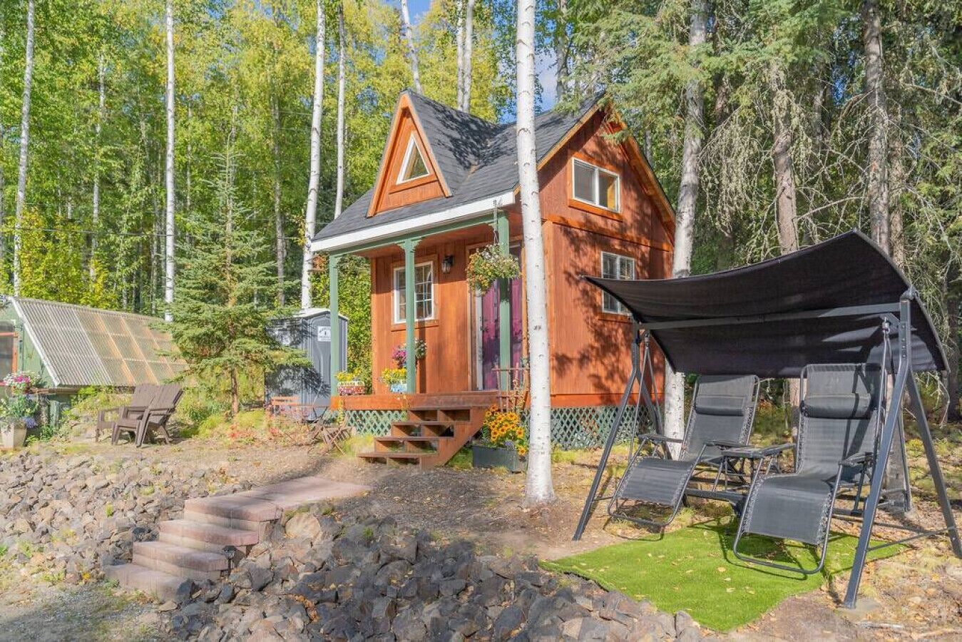 A wooden cabin with a porch, surrounded by trees.