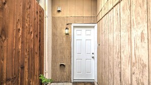 Une ruelle étroite, bordée de murs en bois, avec une porte blanche et une petite lanterne fixée au mur.