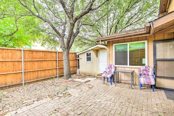 Un jardin avec une clôture en bois, un arbre, une terrasse avec deux chaises et une petite table.