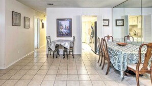 Un espace repas avec une table et des chaises, une cuisine visible à travers une cloison vitrée, et des tableaux encadrés accrochés aux murs.