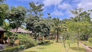 A lush garden with a variety of trees and a small building with a red roof. - Bungalow with king double bed (Krabi)