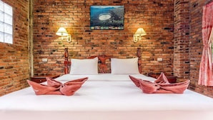 A room with a brick wall, a bed with white linens, two lamps, and a poster of a beach scene. - Bungalow with king double bed (Krabi)