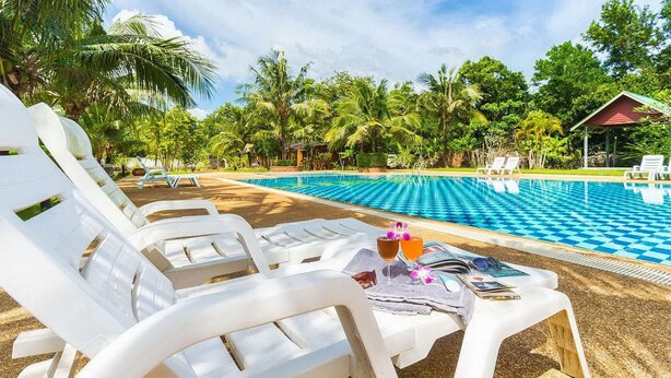 A poolside area with white lounge chairs, a table with drinks and a book, and a pool with a checkered pattern.