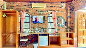 A cozy room with a brick wall, a television, a small refrigerator, and wooden shelves.