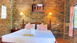 A brick-walled room with a bed, two wall-mounted lamps, and a poster on the wall.