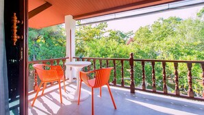 A balcony with two orange chairs and a small table, surrounded by a wooden railing, overlooking a lush green garden.