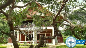A two-story building with a red roof, surrounded by lush greenery and trees.