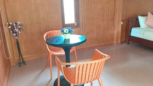 A room with a round table and two chairs, a wooden floor, a window, and a bed with pillows.