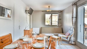 Un'area pranzo con un tavolo di legno apparecchiato per un pasto, una televisione a parete e una finestra con tende.