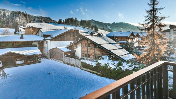 Un villaggio innevato con edifici in legno, una pista da sci sullo sfondo e un cielo azzurro limpido.