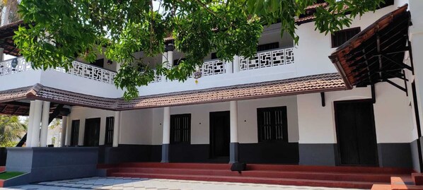 Un edificio de dos pisos con fachada blanca, ventanas de marco negro y techo de tejas rojas.