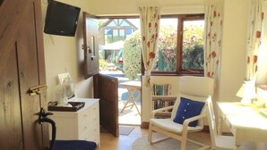 Une pièce confortable avec une chaise blanche, une petite table, une bibliothèque et un téléviseur fixé au mur.