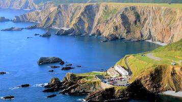 A coastal property with a paved driveway leading to a parking area, a grassy area, and a view of the sea and cliffs.