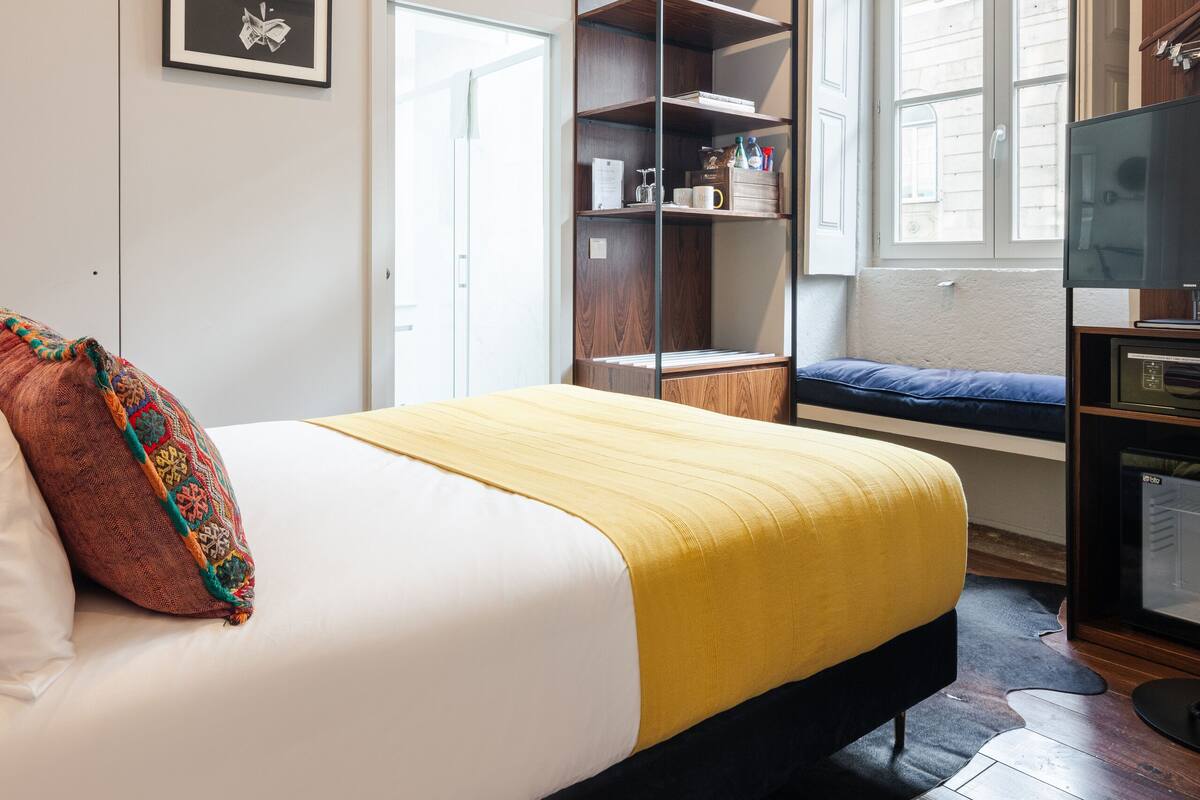 Une chambre à coucher comprenant un lit, un coin fenêtre aménagé en siège, une armoire et un téléviseur.