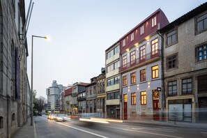 A street view with multi-story buildings, a clear sky, and moving vehicles creating light trails. - Utopian - Design Suites Porto (Porto)