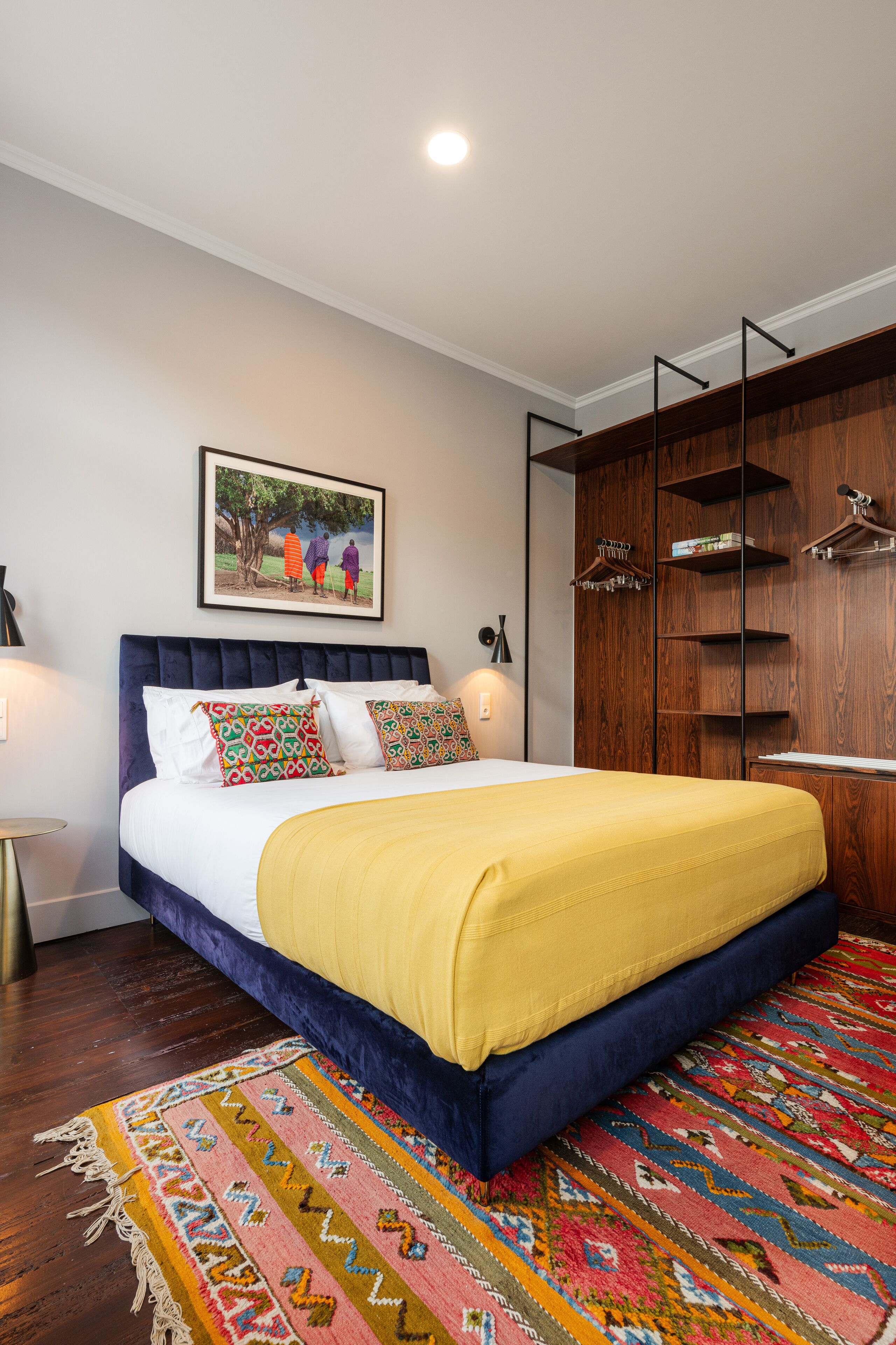 Une chambre à coucher avec un grand lit, une armoire en bois, un tapis coloré et un tableau encadré au mur.
