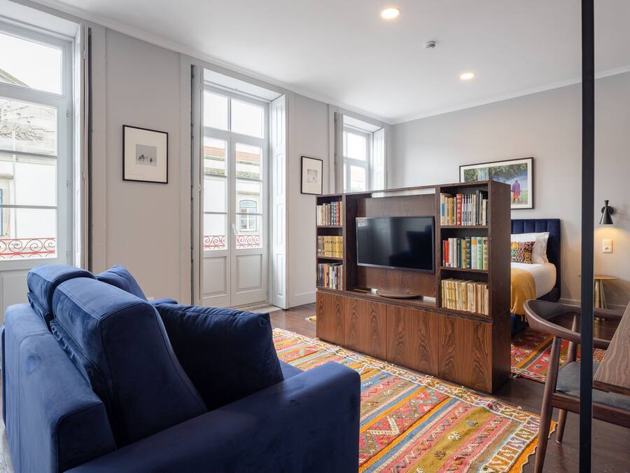 A living room with a blue sofa, a TV on a wooden stand, and a bookshelf.