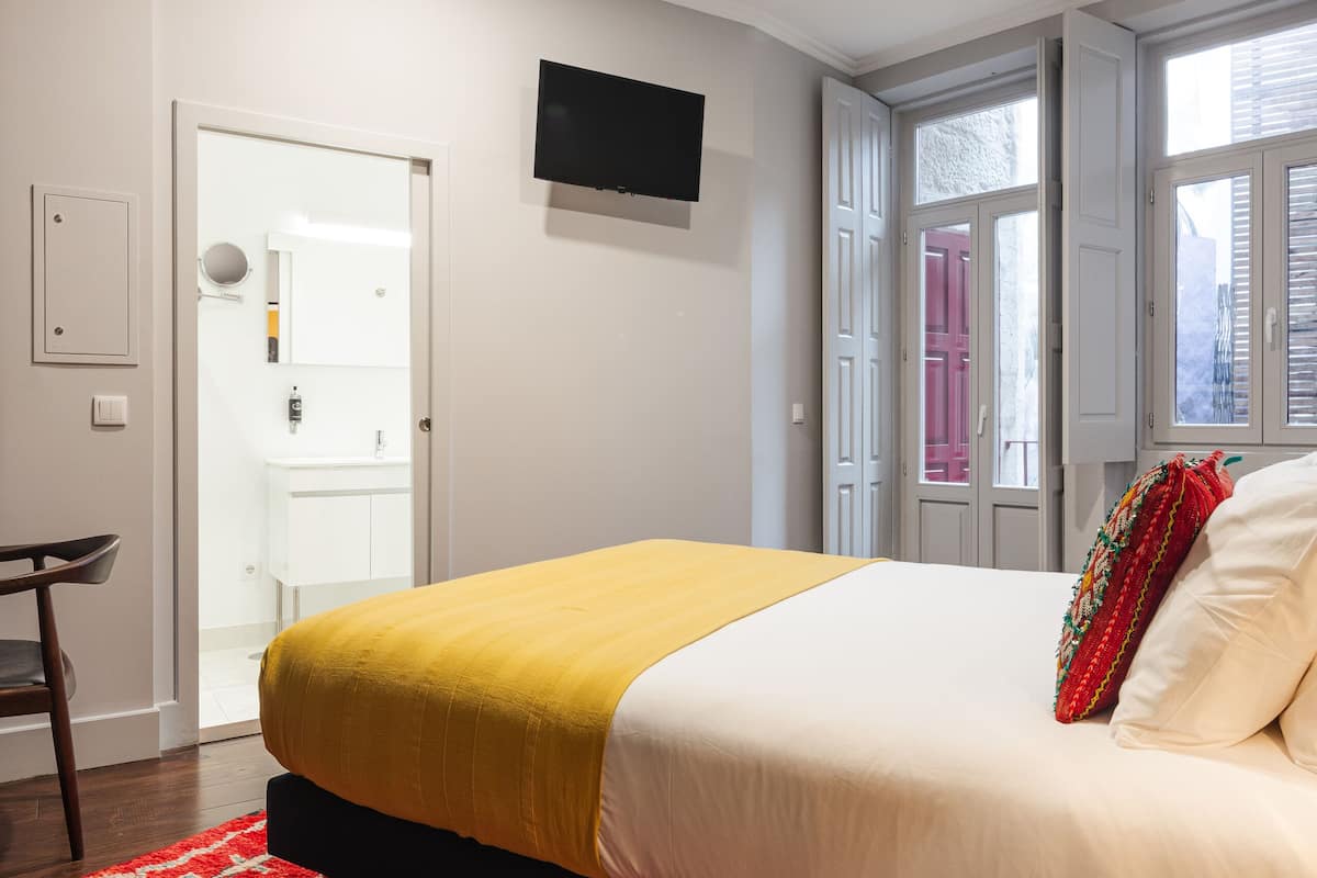 Une chambre à coucher avec un lit, un téléviseur fixé au mur et une porte donnant sur une salle de bain.