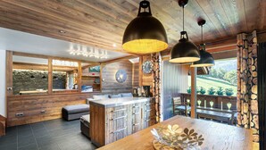 A modern kitchen with wooden accents, a central island, pendant lighting, and a view of the outdoors. - Modern Duplex in Méribel Village, ski-in/ski-out access and pool (Méribel)
