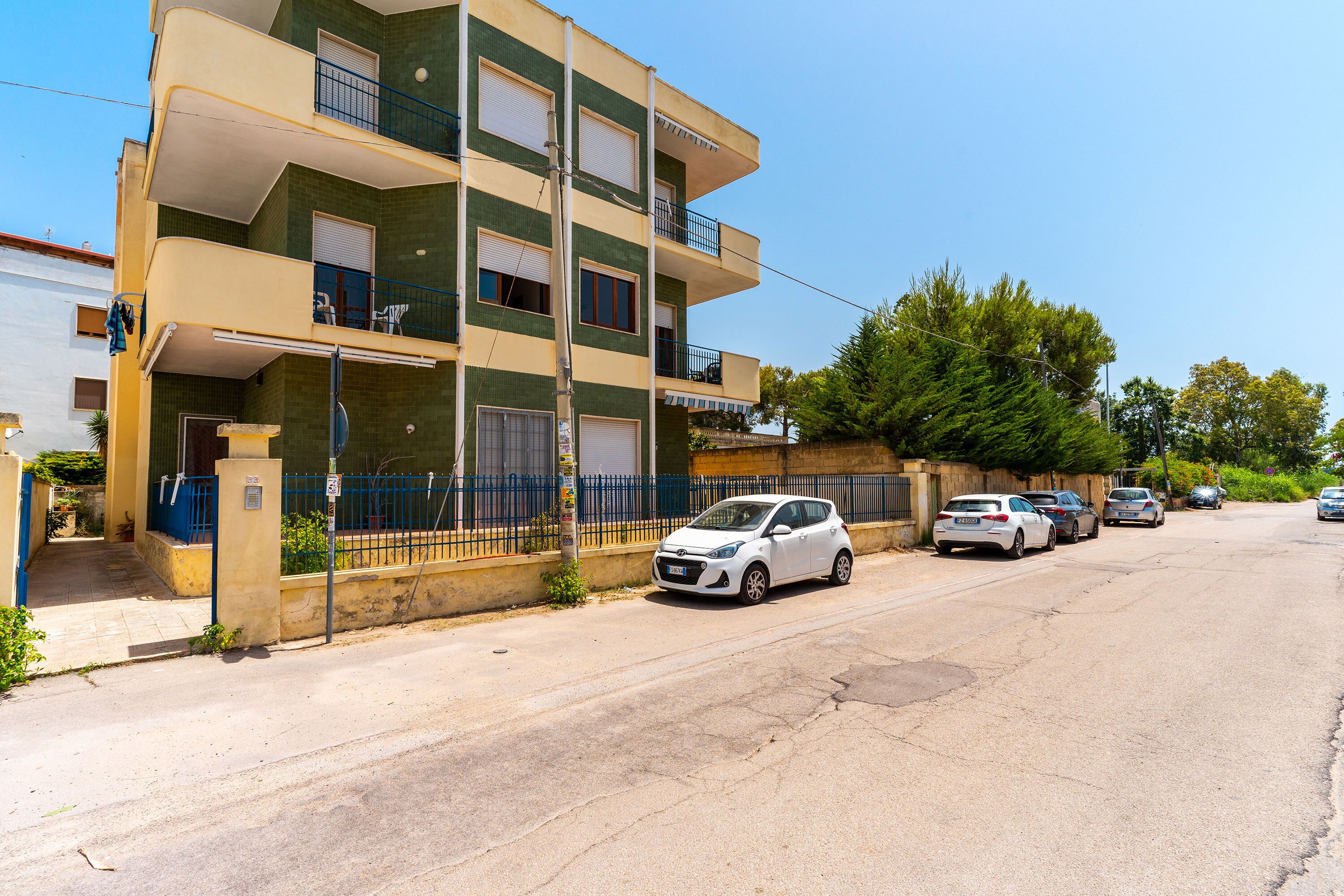 Un edificio residencial de varios pisos con balcones, zona de estacionamiento y cielo despejado.
