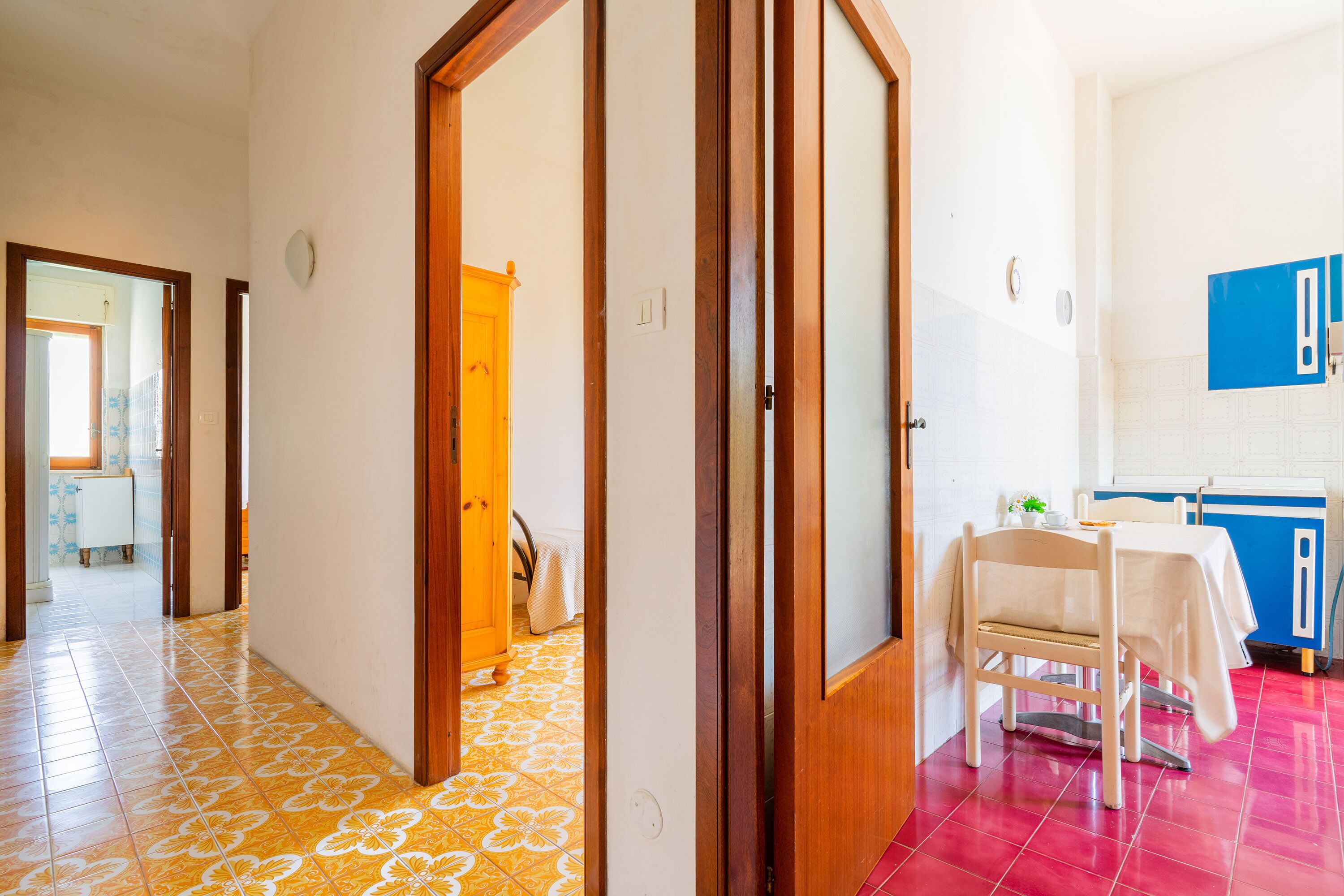 A hallway with a wooden door, a dining area with a table and chairs, and a kitchen area with blue cabinets.