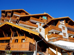 Een houten chalet met meerdere verdiepingen, balkons en een gevel van steen.